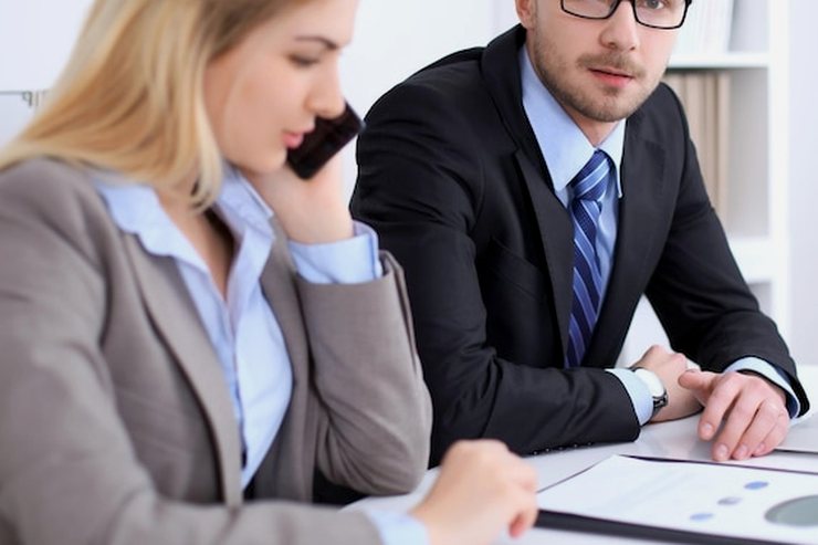 A man at a laptop beside a colleague taking a phone call