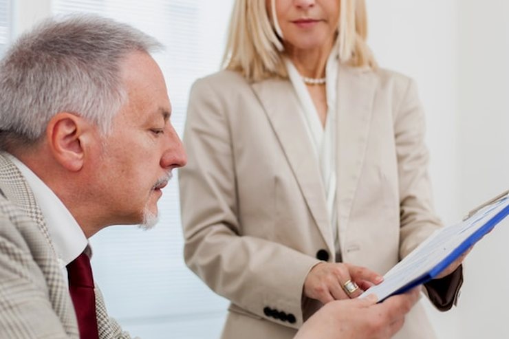 A woman holding a folder open while an older colleague reads it